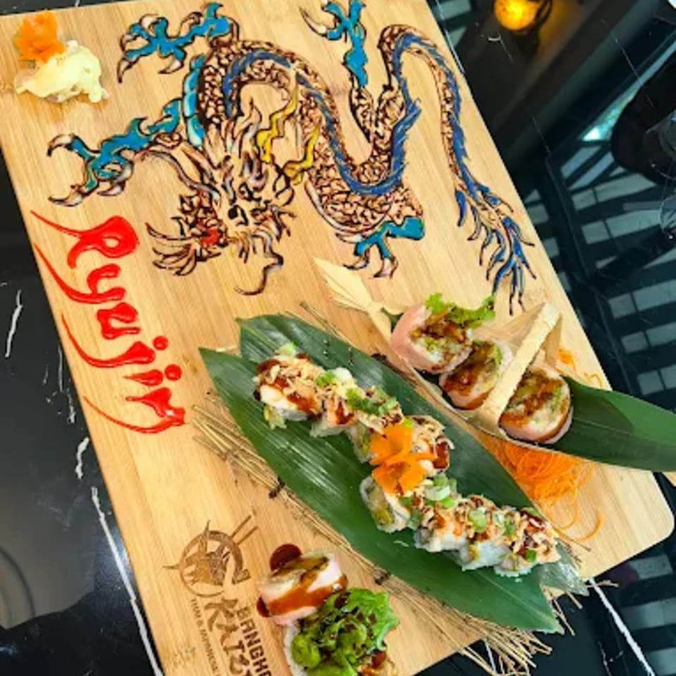 Sushi rolls and sashimi artfully arranged on a wooden board with a painted dragon design.
