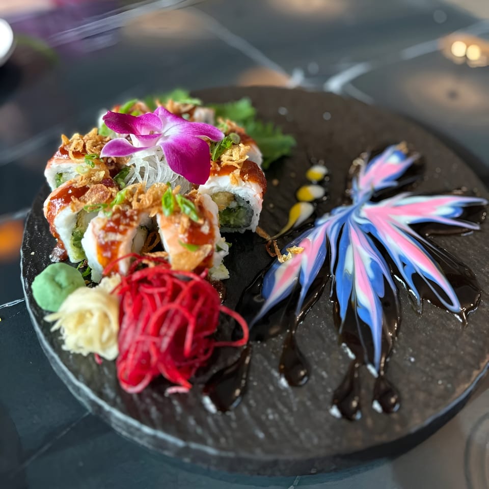 Sushi rolls with crispy toppings and a purple orchid, alongside colorful sauce art on a dark plate.