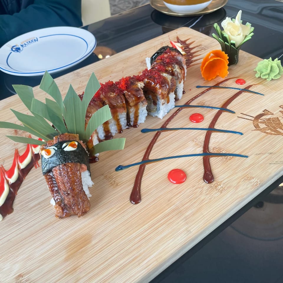Dragon sushi roll with eel, roe, and decorative sauces on a wooden board at Bangkok Kaizen.