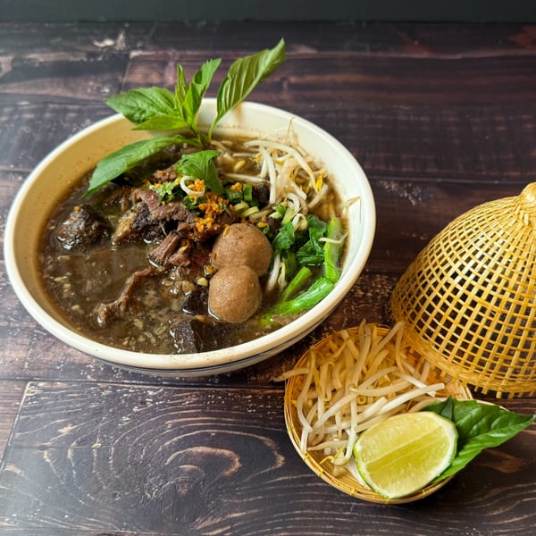 Thai boat noodles with beef, meatballs, bean sprouts, and basil, served with lime.