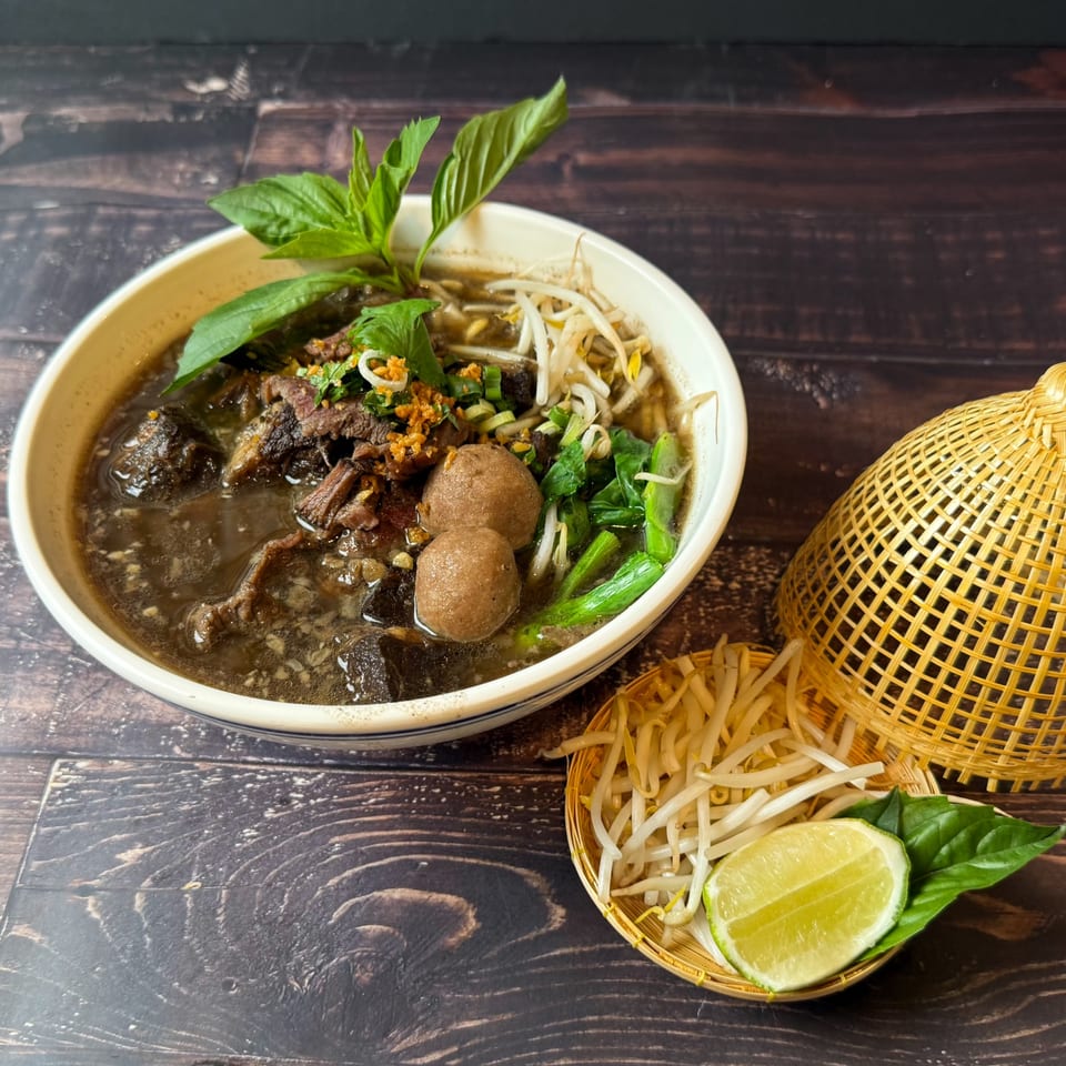 Thai boat noodles with beef, meatballs, bean sprouts, and basil, served with lime.
