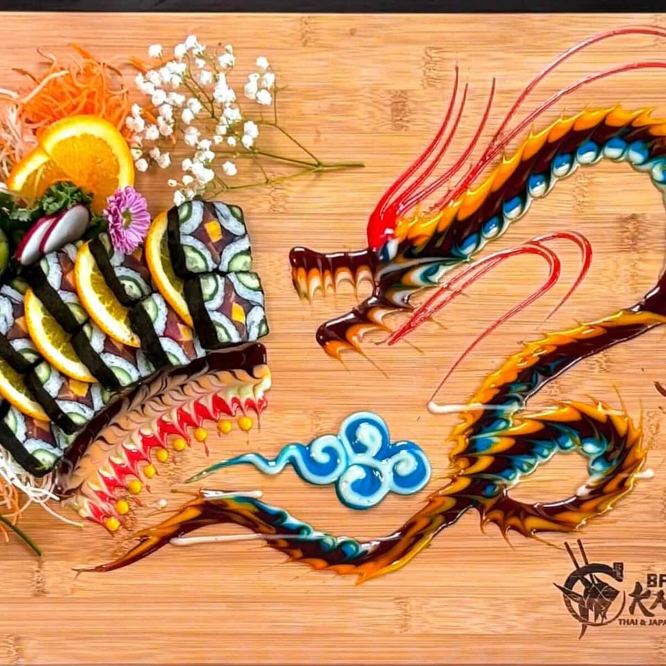 Dragon-shaped sushi platter with colorful sauces, orange slices, and baby's breath on a wooden board.