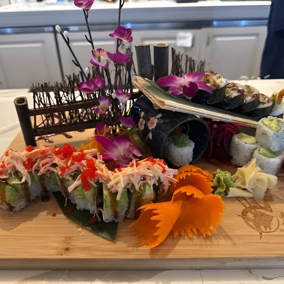 Assorted sushi rolls, including crab and avocado, artfully arranged with orchids and carved carrots on a wooden board.