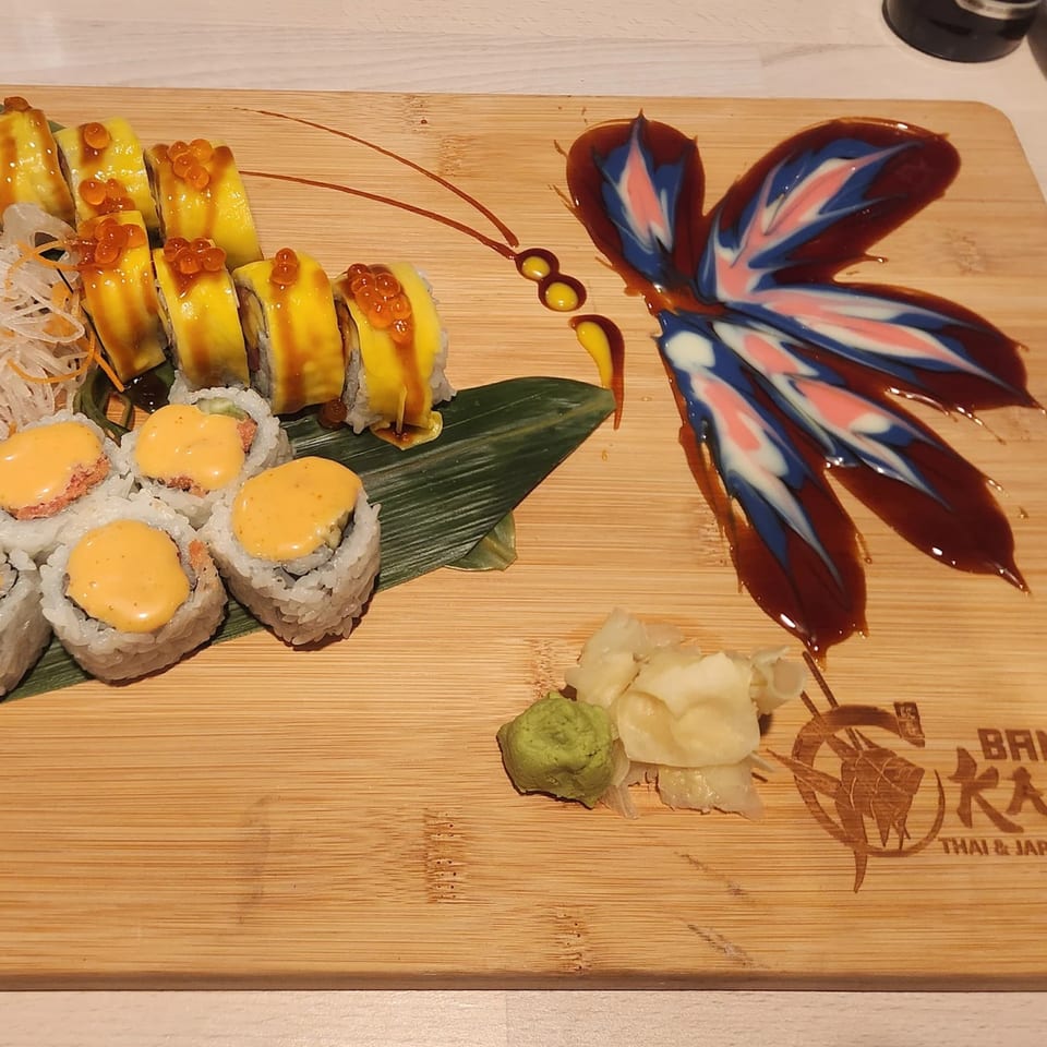 Sushi rolls with yellow topping and orange roe, with wasabi and ginger on a wooden board.