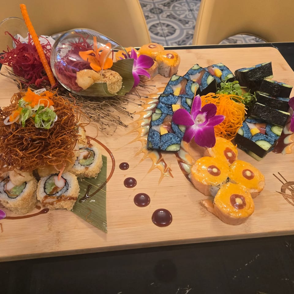 A large wooden platter with various colorful sushi rolls, garnishes, and sauces.