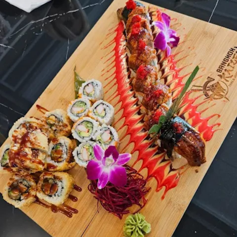 A wooden board with various sushi rolls, including dragon rolls, decorated with red sauce and orchids.