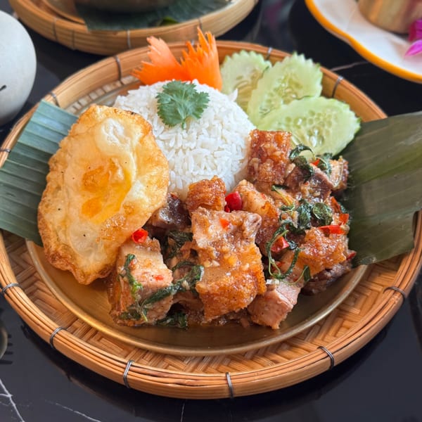 Crispy pork belly with basil, rice, fried egg, and cucumber on a bamboo tray at Bangkok Kaizen.