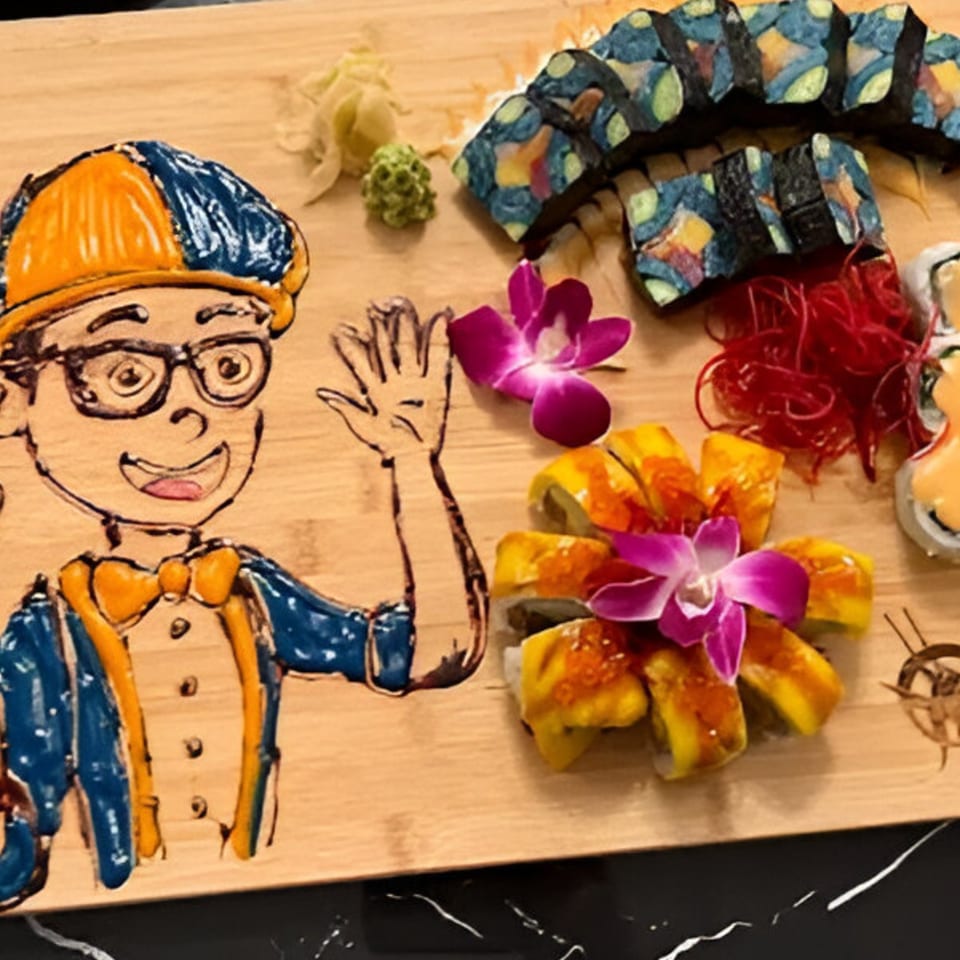 Sushi platter with a cartoon character drawing, colorful rolls, and purple orchid garnishes on a wooden board.