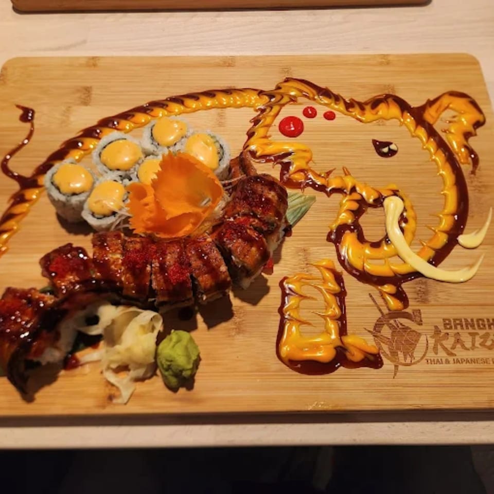 Sushi rolls and sashimi on a wooden board, with sauces forming an elephant design.