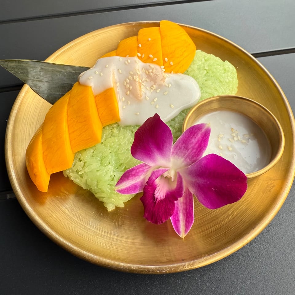 Mango sticky rice with coconut milk, sesame seeds, and an orchid on a golden plate.