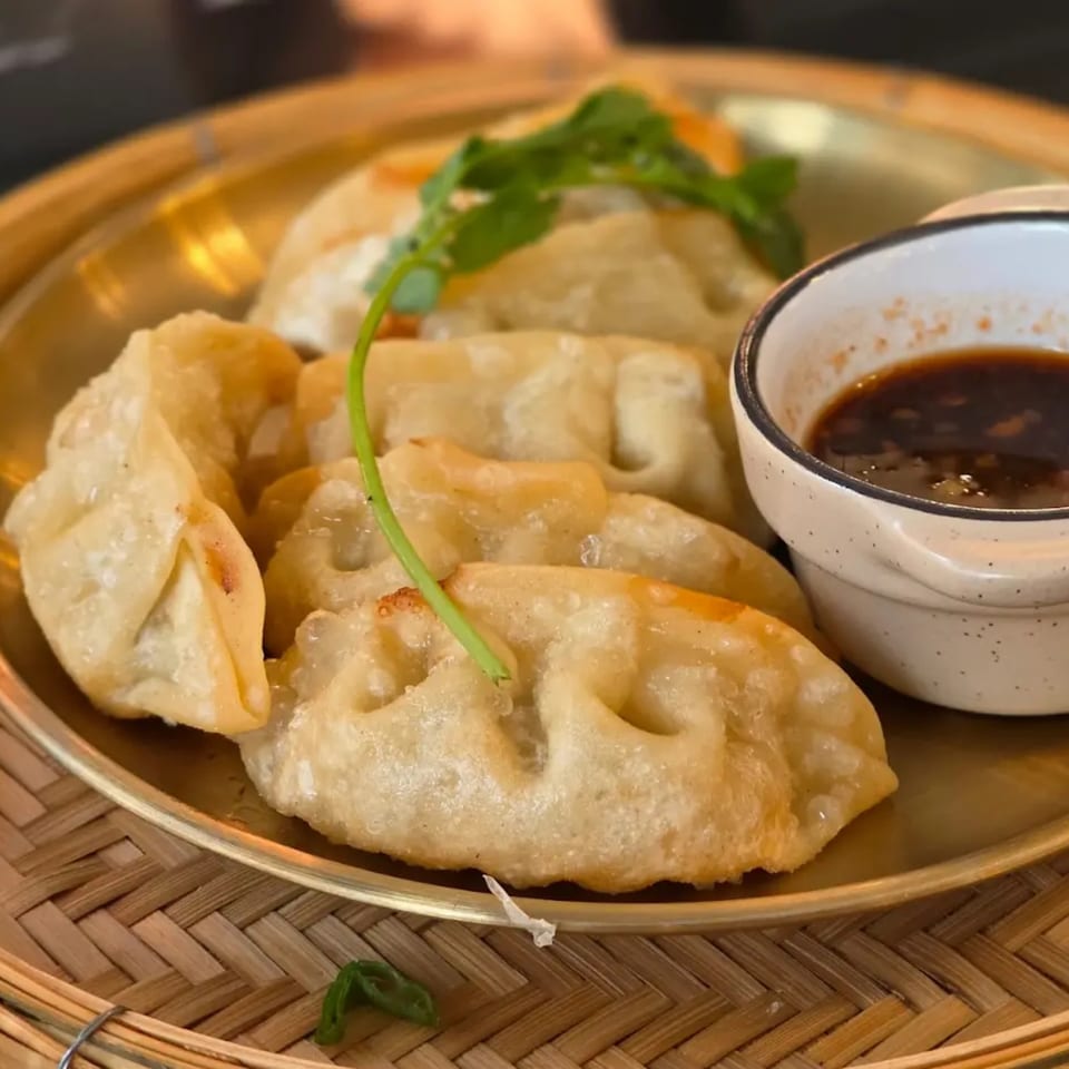 Golden-fried dumplings with a sprig of cilantro and a side of dipping sauce on a brass plate.