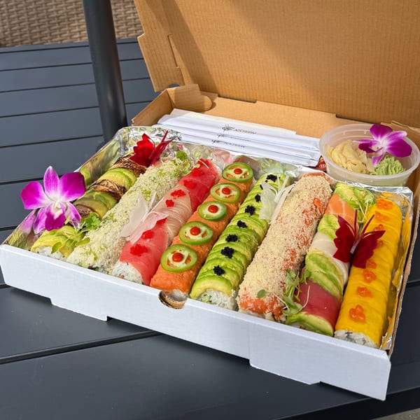 Colorful sushi rolls with various toppings and garnishes, including orchids, in a takeout box.