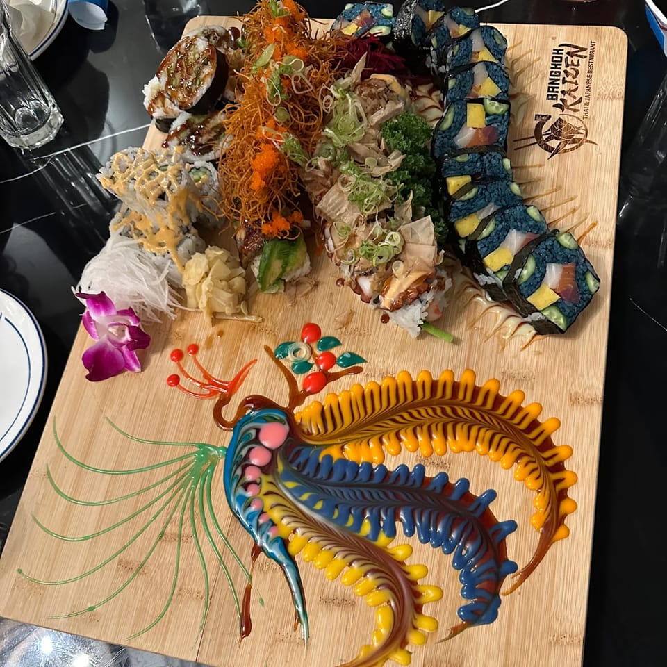 A large wooden board with various sushi rolls and a colorful sauce dragon design.
