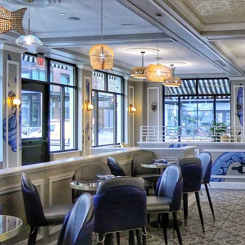 Interior of Bangkok Kaizen restaurant with blue chairs, round tables, and large windows.
