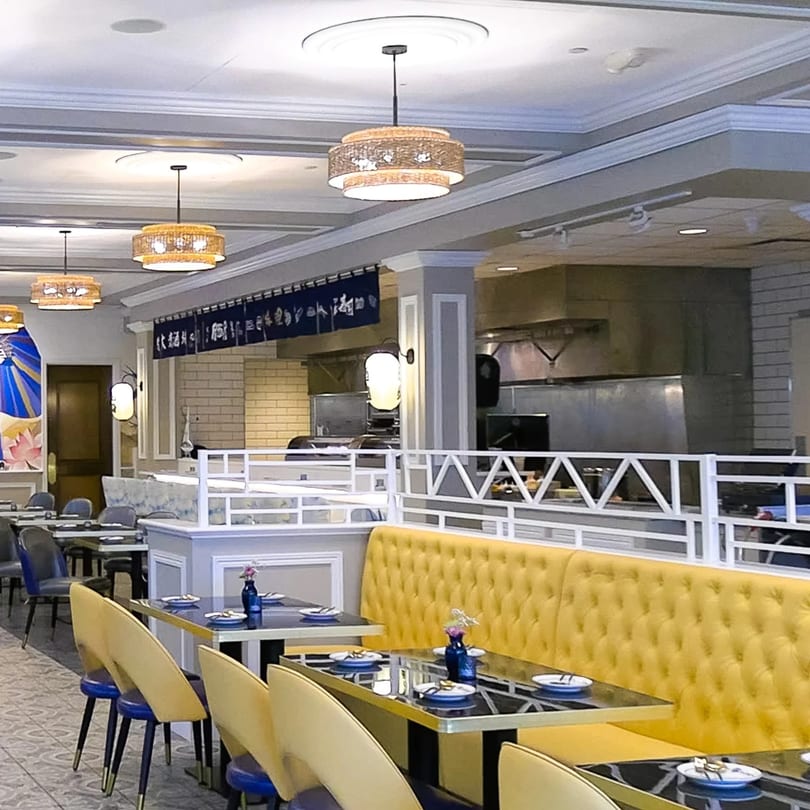 Modern Thai restaurant interior with yellow booth seating, black tables, and decorative hanging lights.