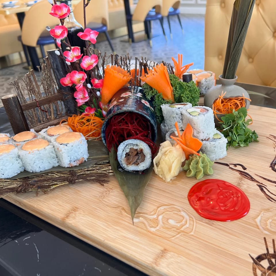 A vibrant sushi platter with various rolls, garnishes, and sauces on a wooden board.